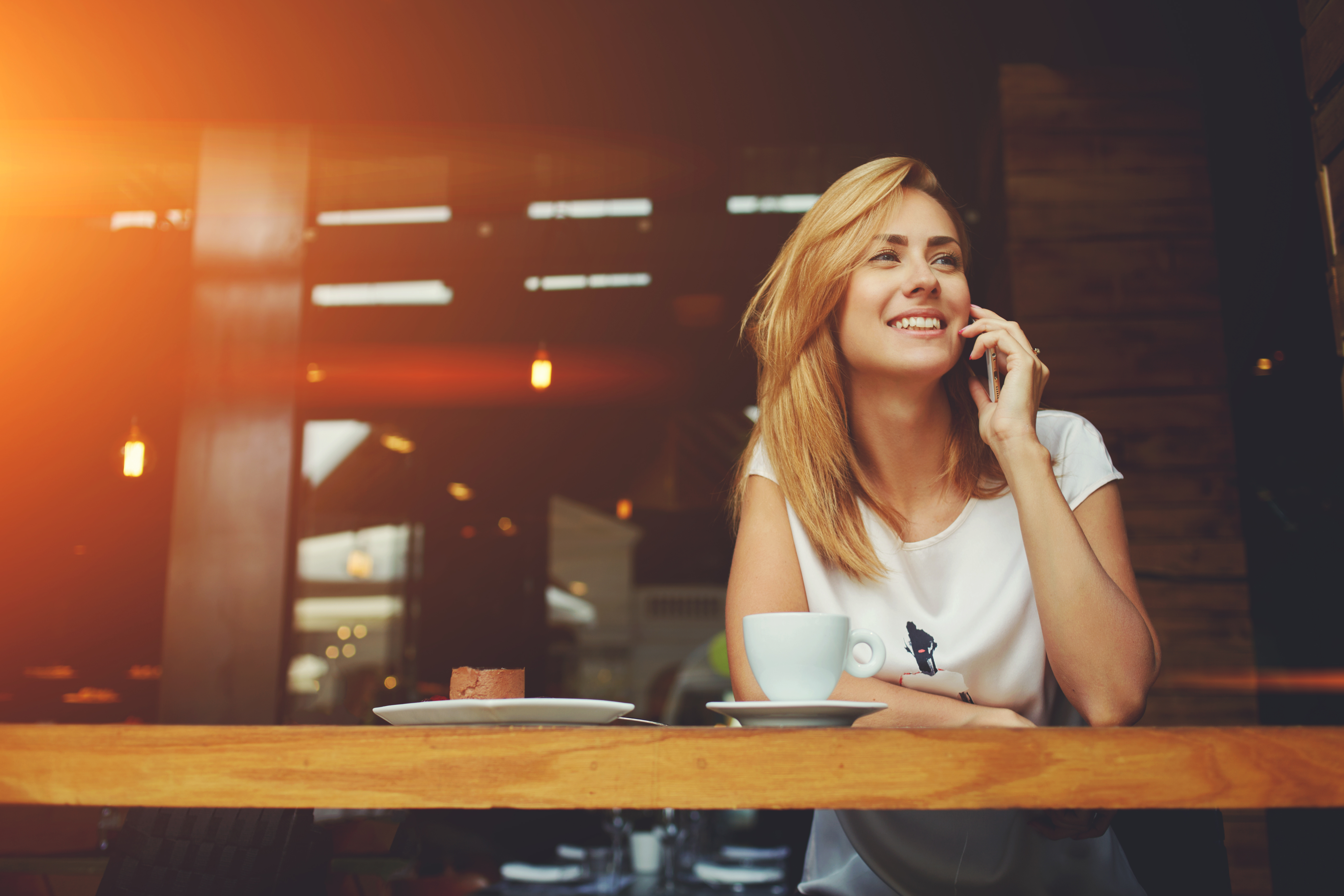 Young charming woman calling with cell telephone while sitting alone in coffee shop during free time, attractive female with cute smile having talking conversation with mobile phone while rest in cafe