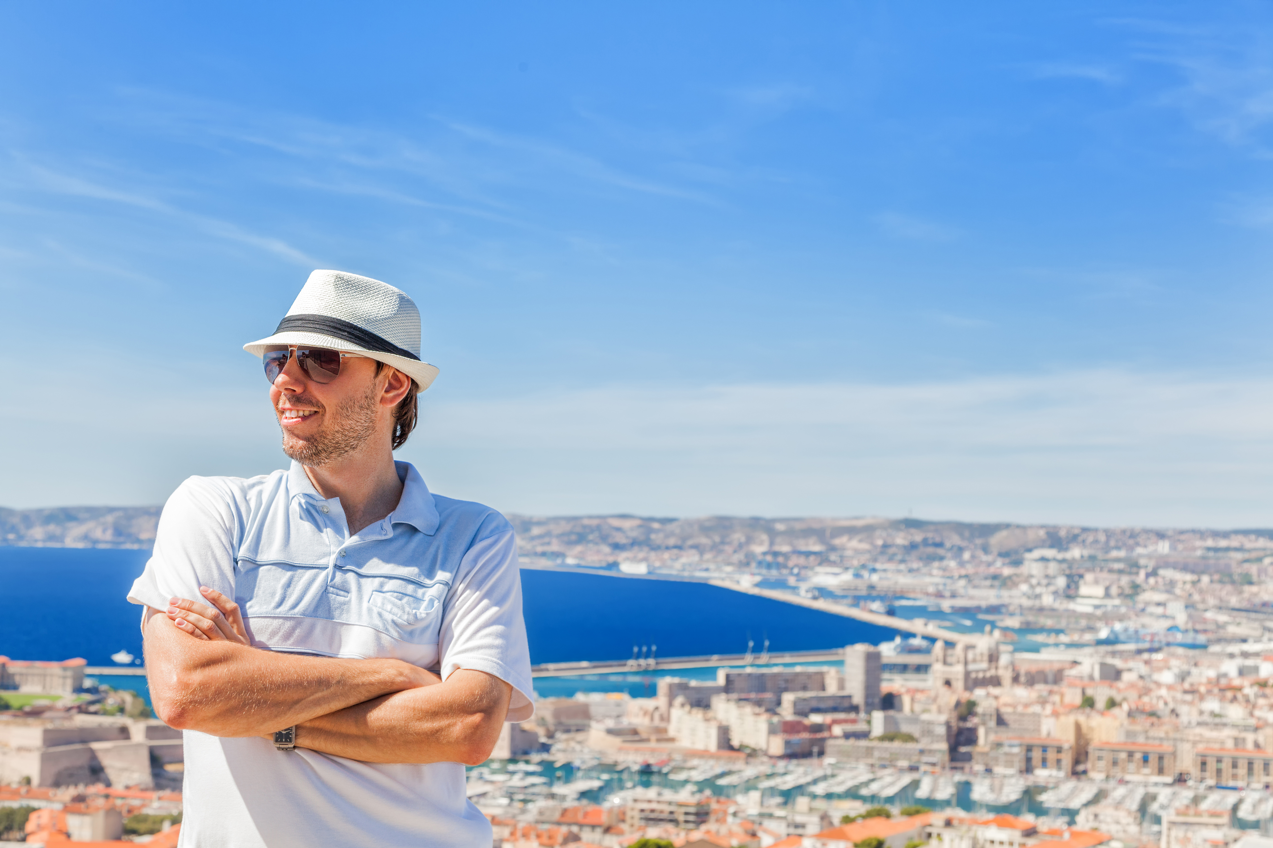 Happy traveling! Handsome man in a hat and sunglasses posing against the city of Marseille