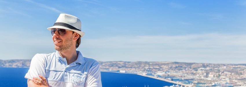 Happy traveling! Handsome man in a hat and sunglasses posing against the city of Marseille