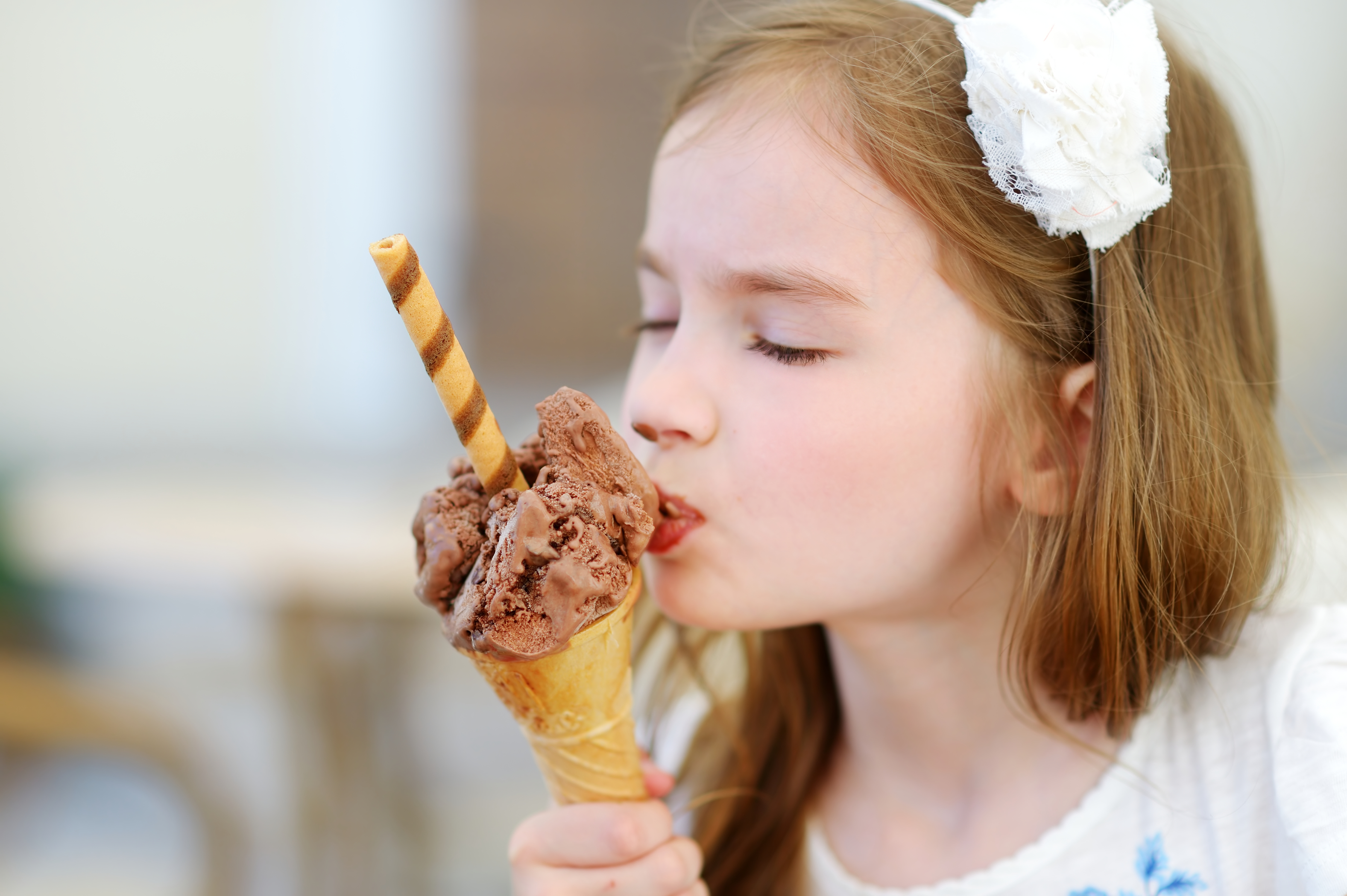 Adorable little girl eating tasty fresh ice cream outdoors on warm sunny summer day