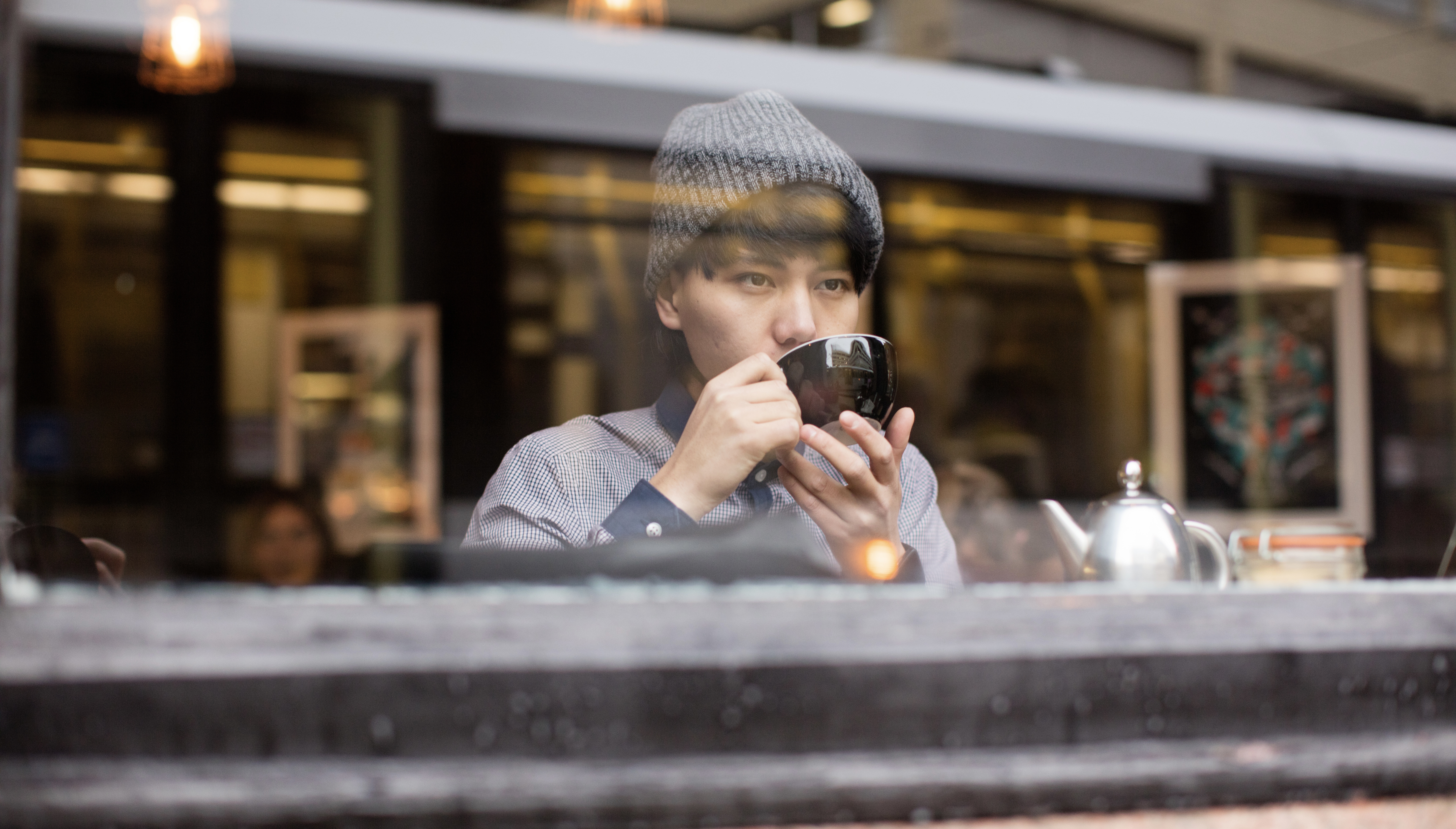 Young asian male drinking tea in cafe whilst looking out of window