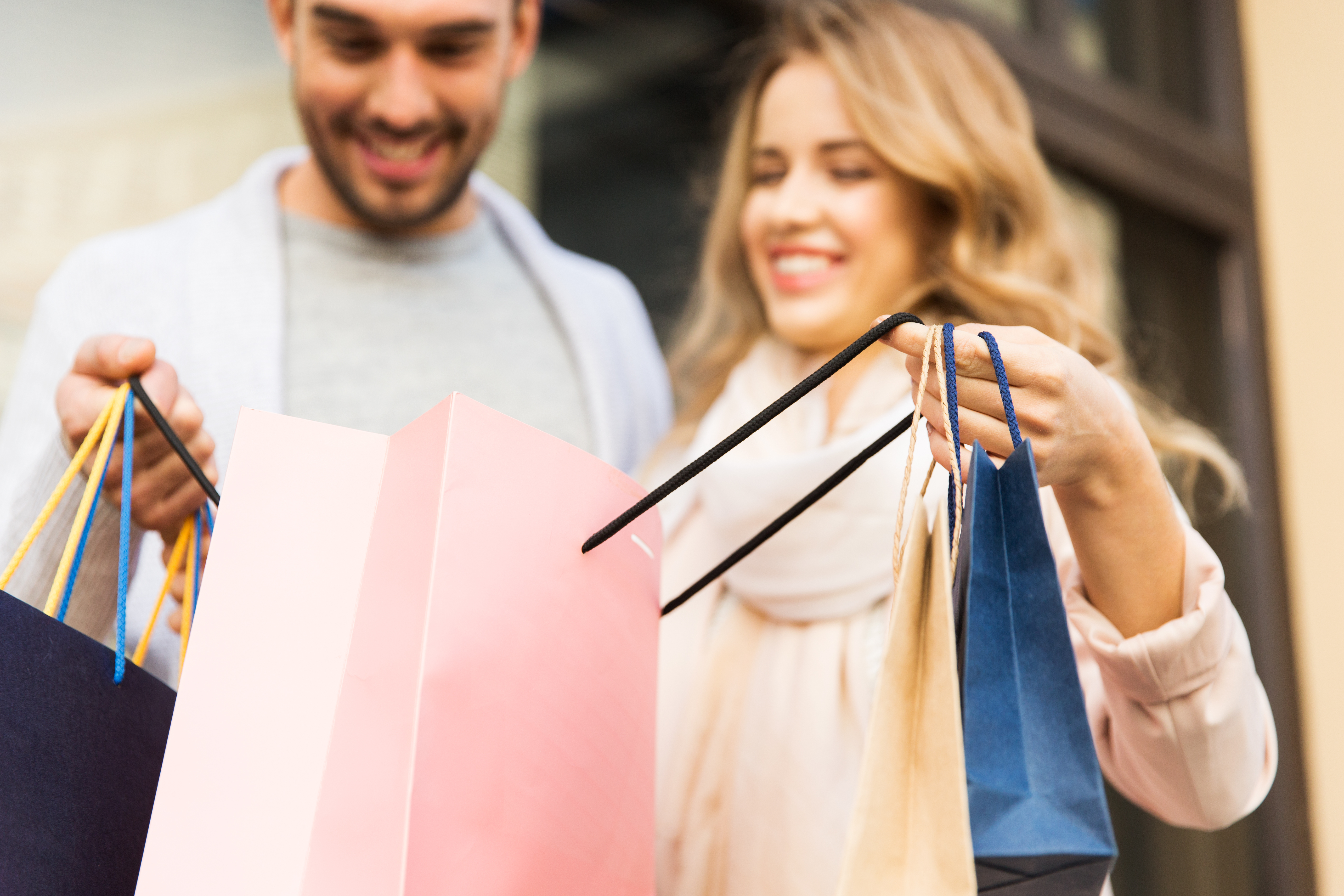 sale, consumerism and people concept - close up of happy couple looking into shopping bag at shop window on city street
