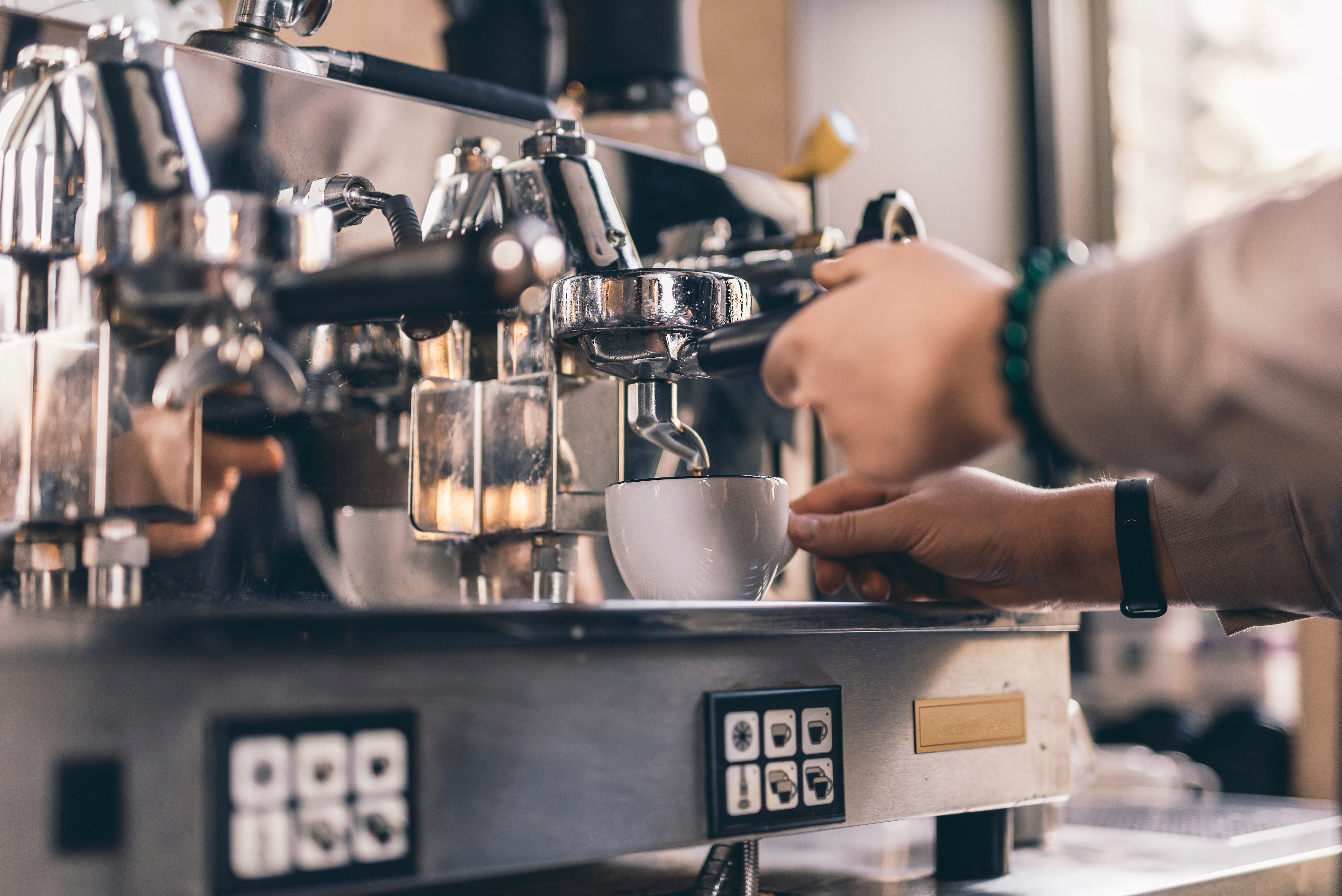 Close up photo of experienced barista touching a cup and a filter holder while pouring coffee from espresso machine