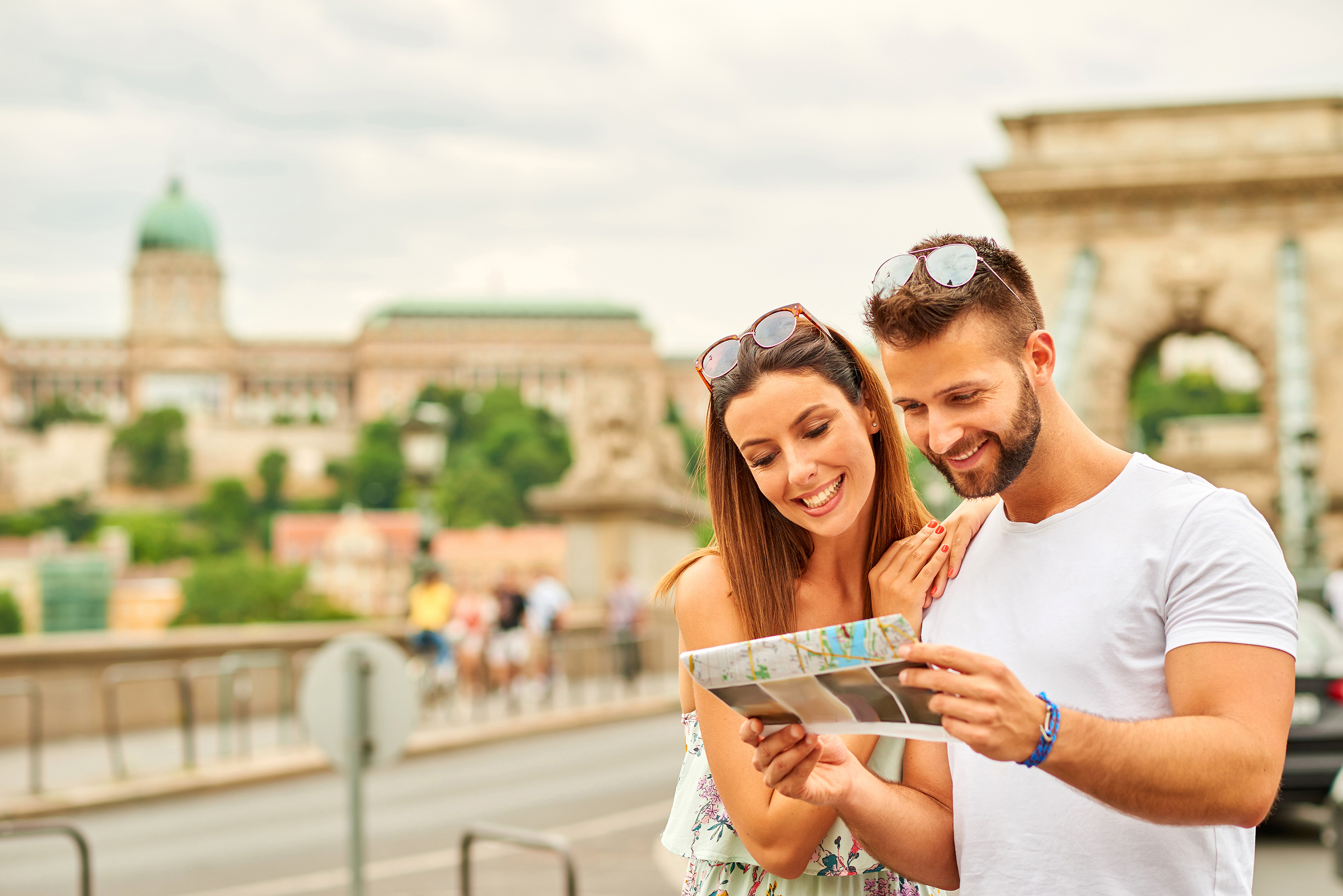 A young couple looking at a map with the castle of Buda and the Chain Bridge behind them in Budapest, Hungary.