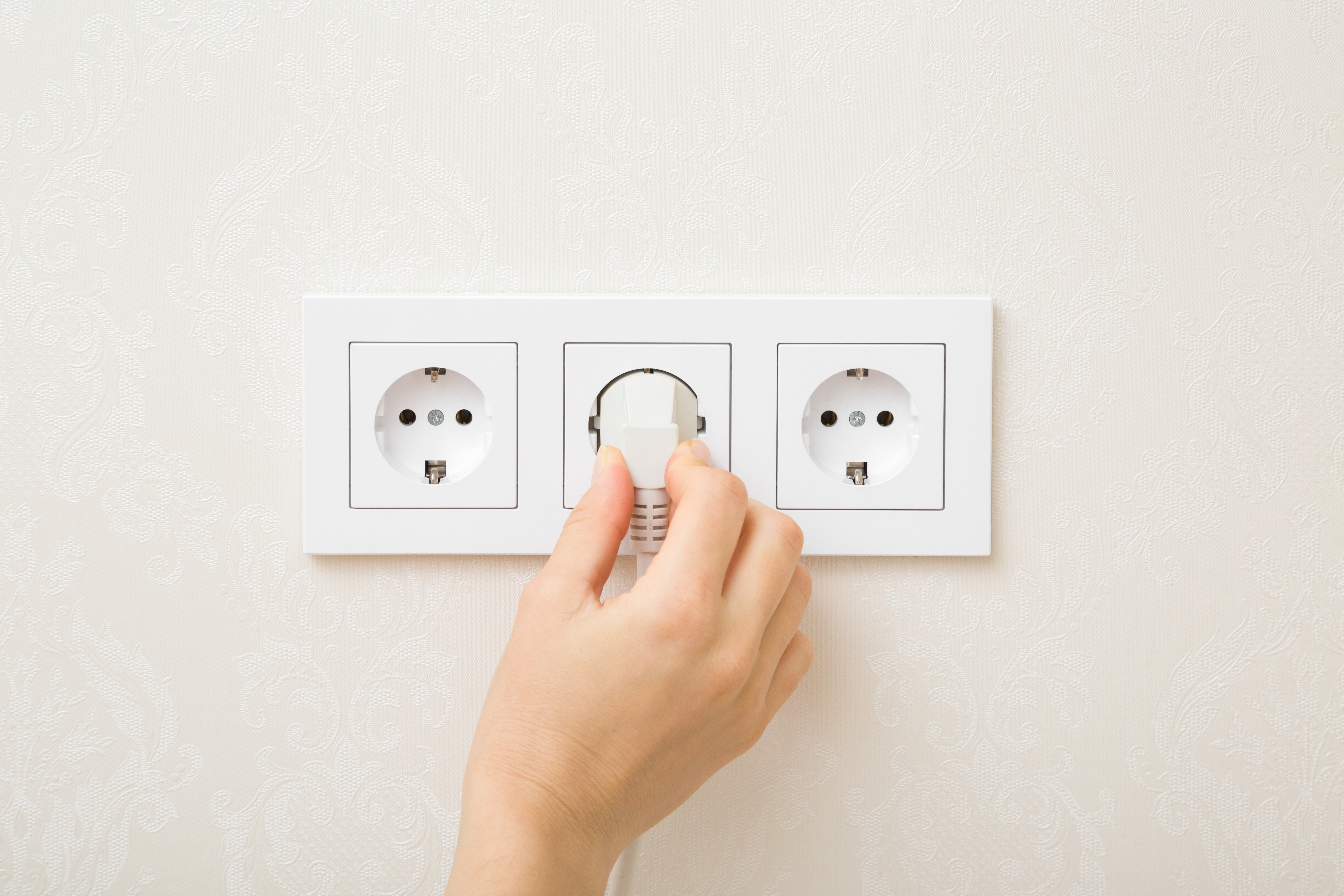woman hand holding and plugging white electrical plug in wall outlet socket at home