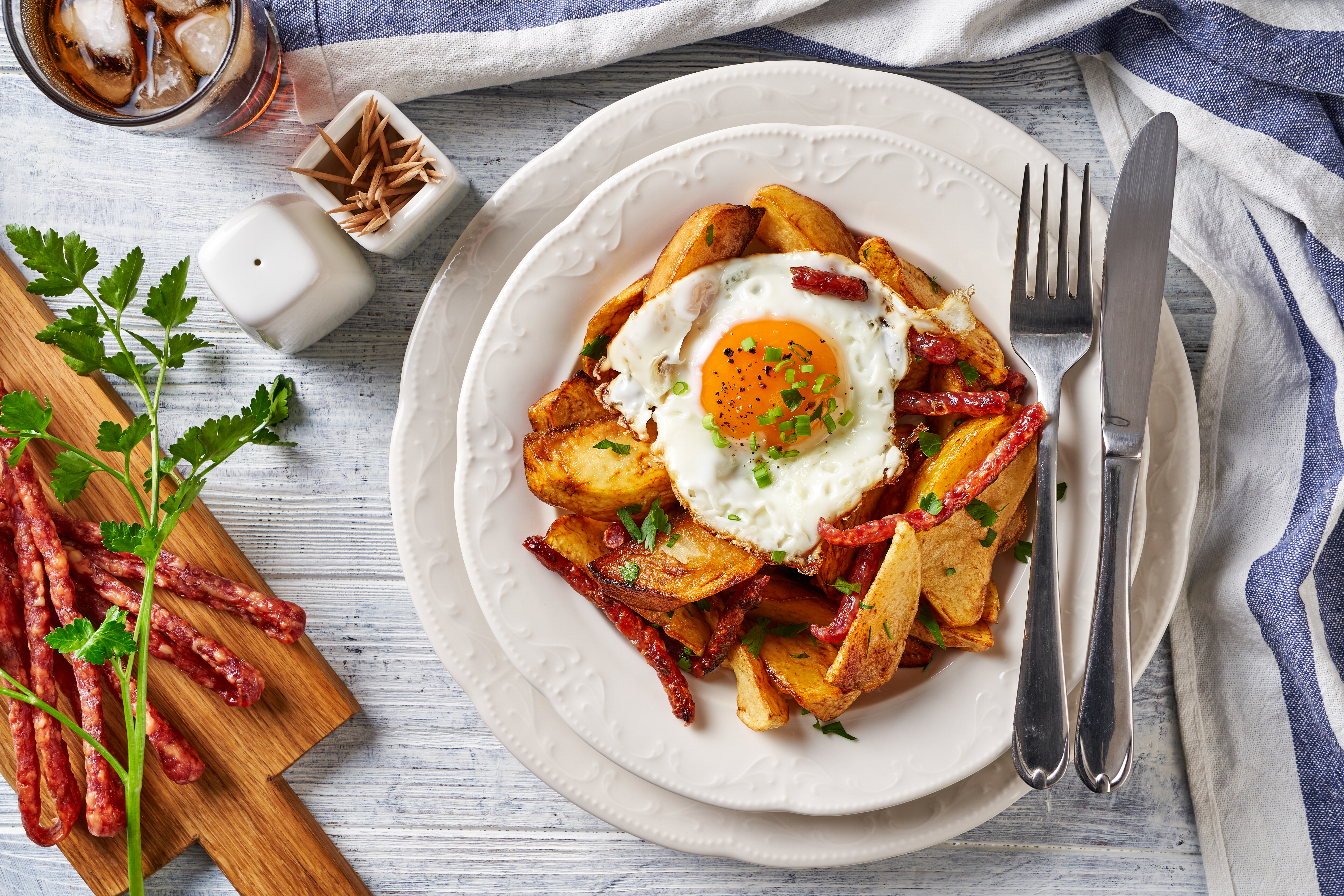 Spanish breakfast dish huevos rotos or broken eggs of crispy french fries, fried eggs, spanish dry cured sausage chistorra.