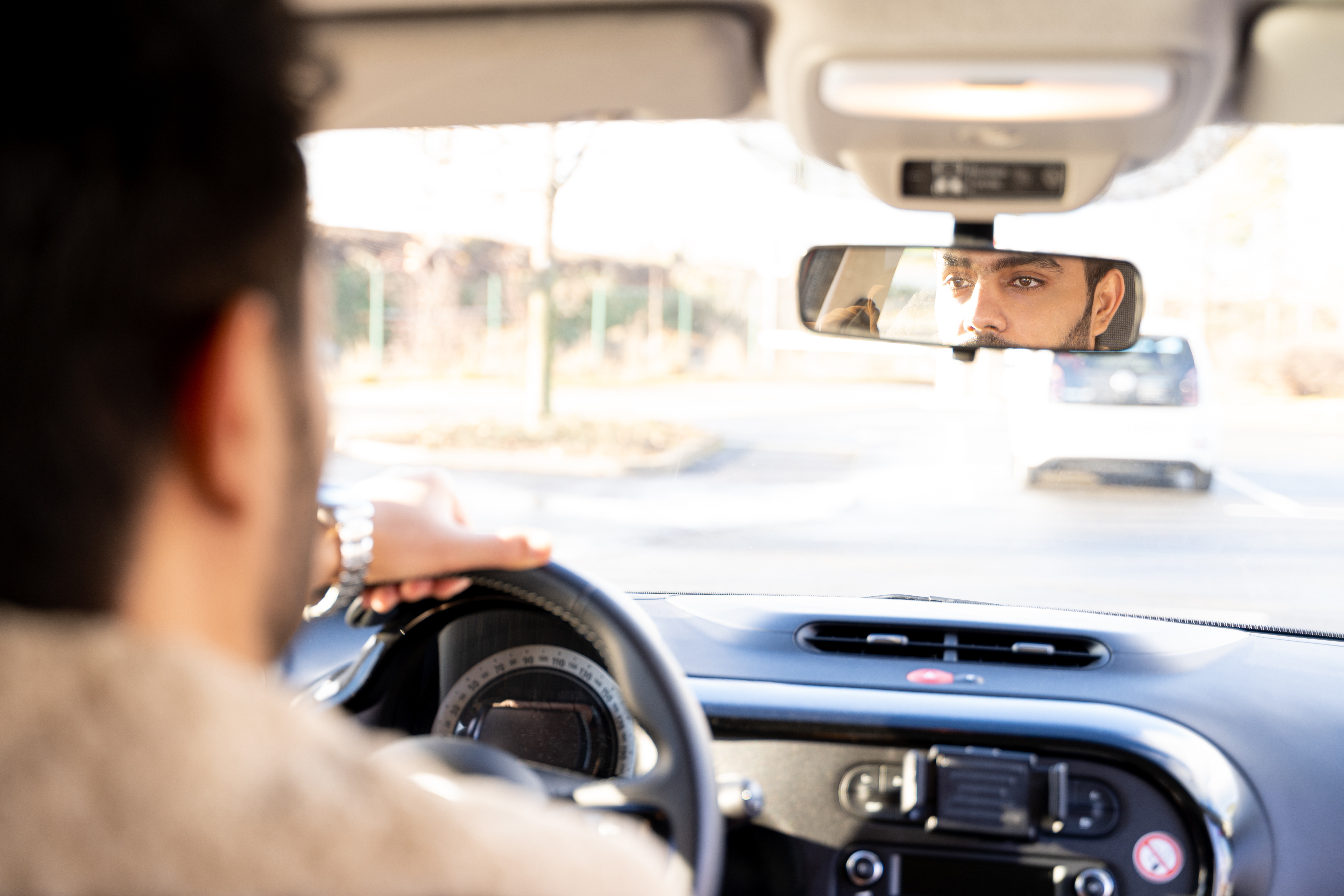 Man with hands holding driving wheel riding car on sunny autumn, winter or spring day.