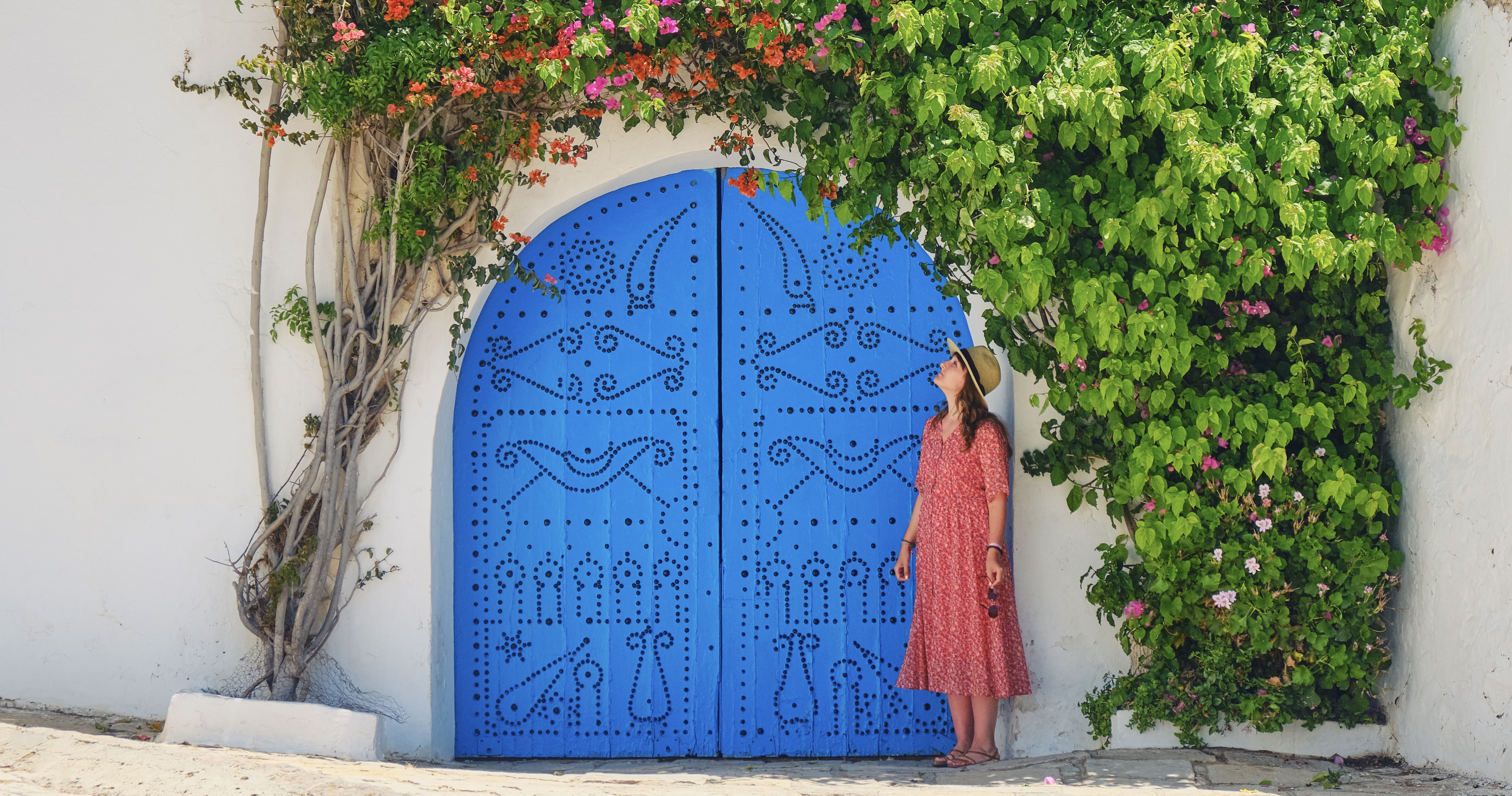 Woman next to home entwined liana with flowers in Sidi Bou Said, Tunisia