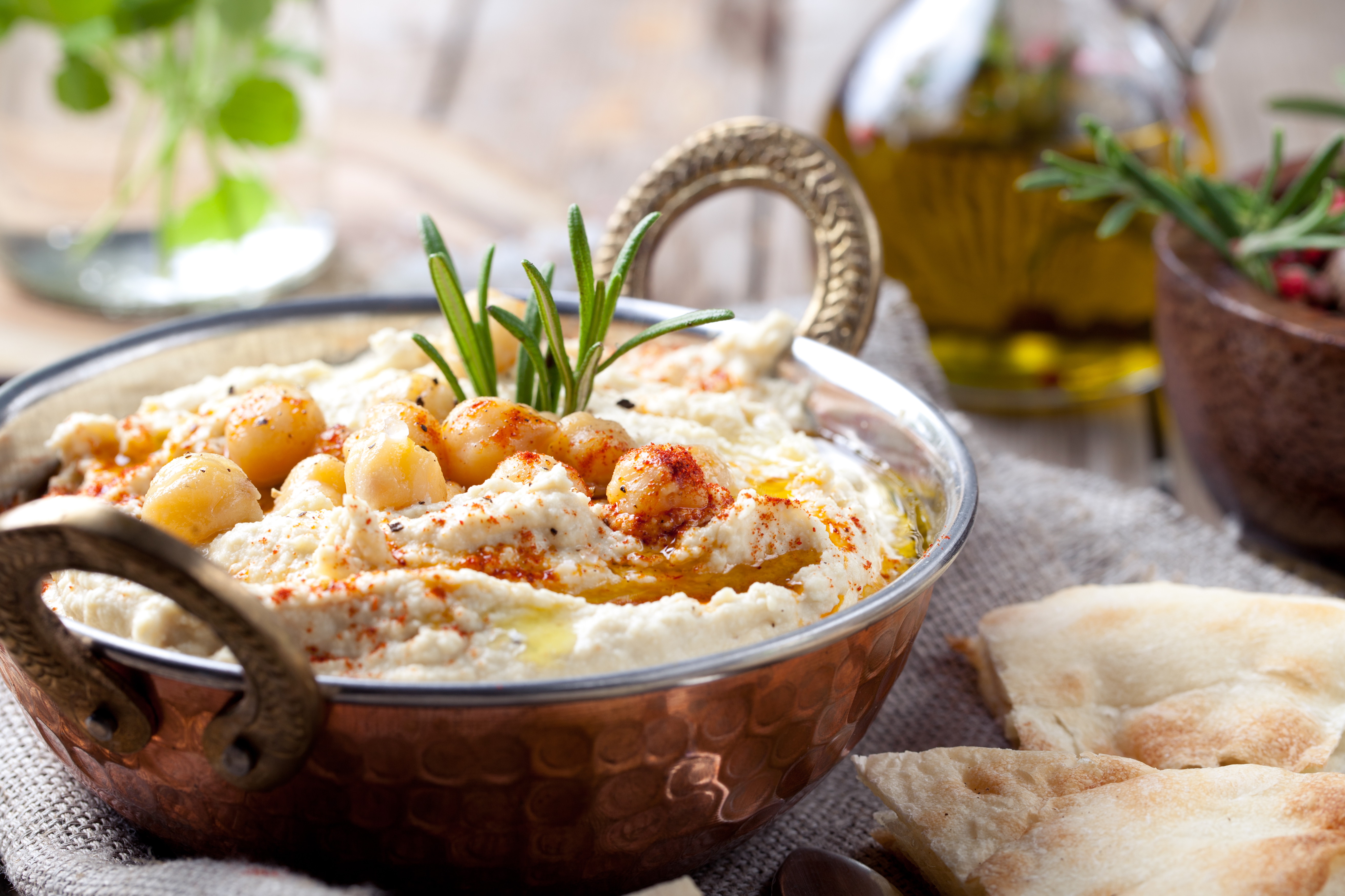 Hummus, chickpea dip, with rosemary, smoked paprika and olive oil in a metal authentic bowl with pita on a wooden background.