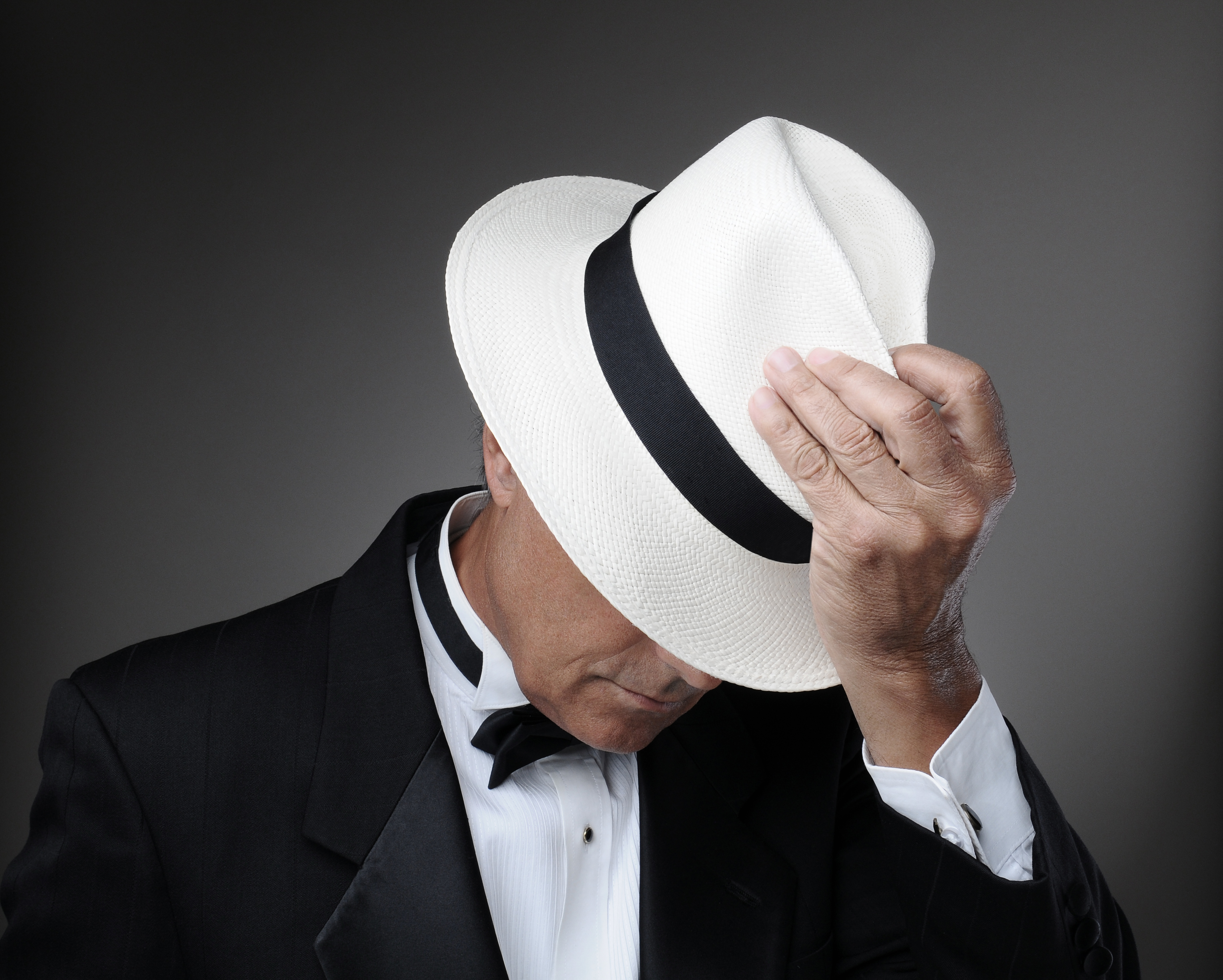 Closeup of a middle aged man wearing a tuxedo and a Panama Hat. Horizontal over a gray background.
