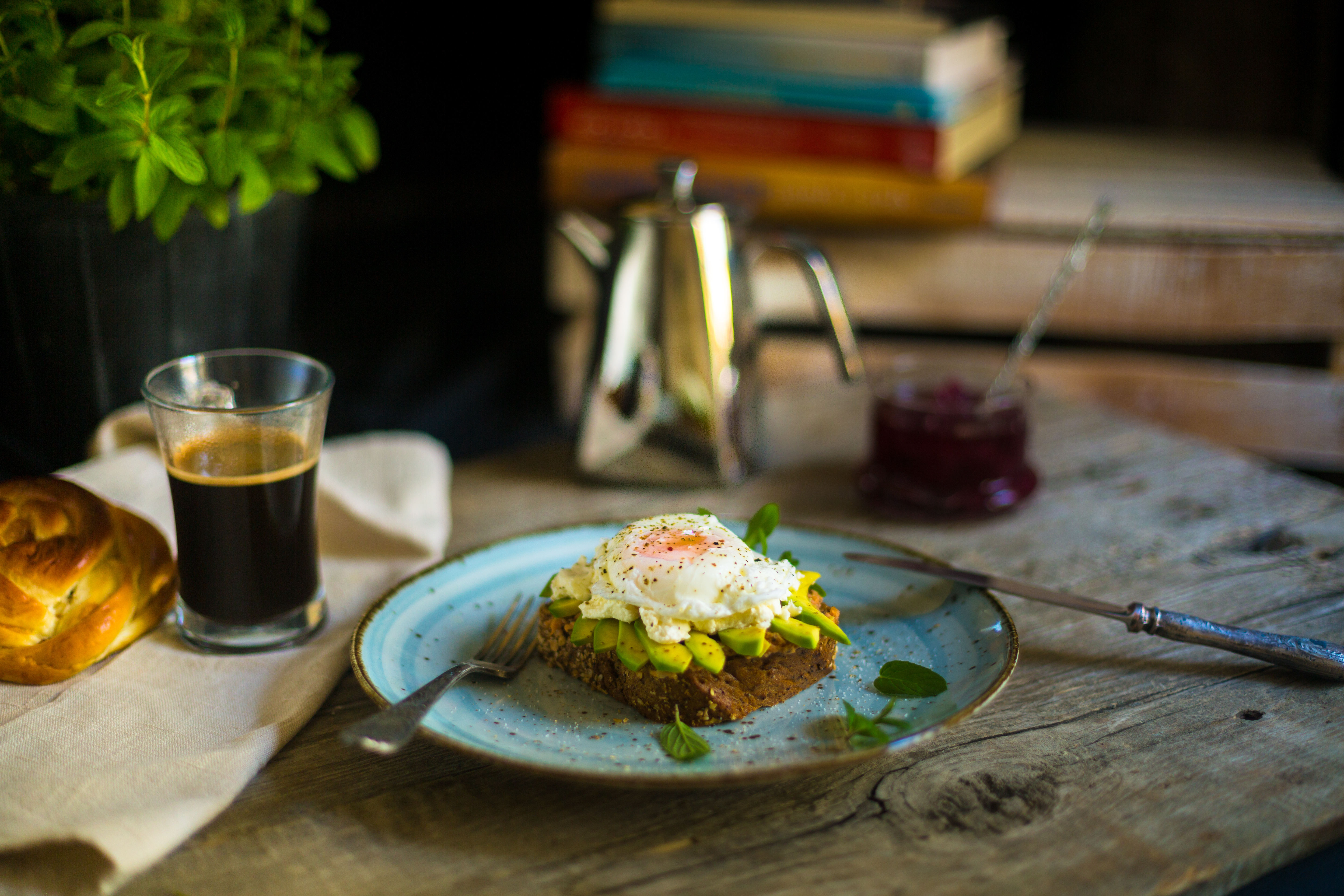 Black bread toast with fried egg, avocado and salmon spread in blue plate with coffee in background