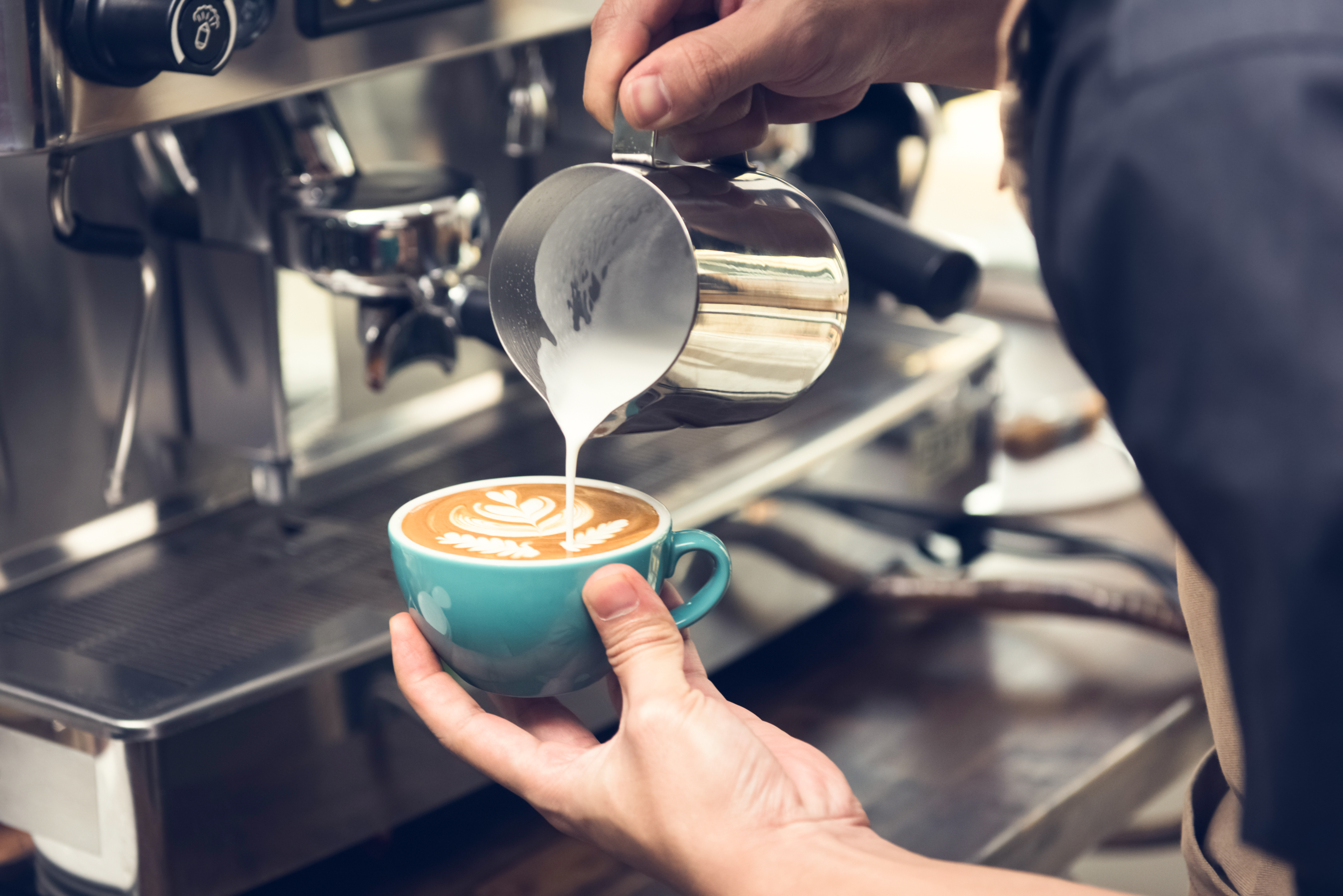 Professional barista pouring steamed milk into coffee cup making beautiful latte art Rosetta pattern