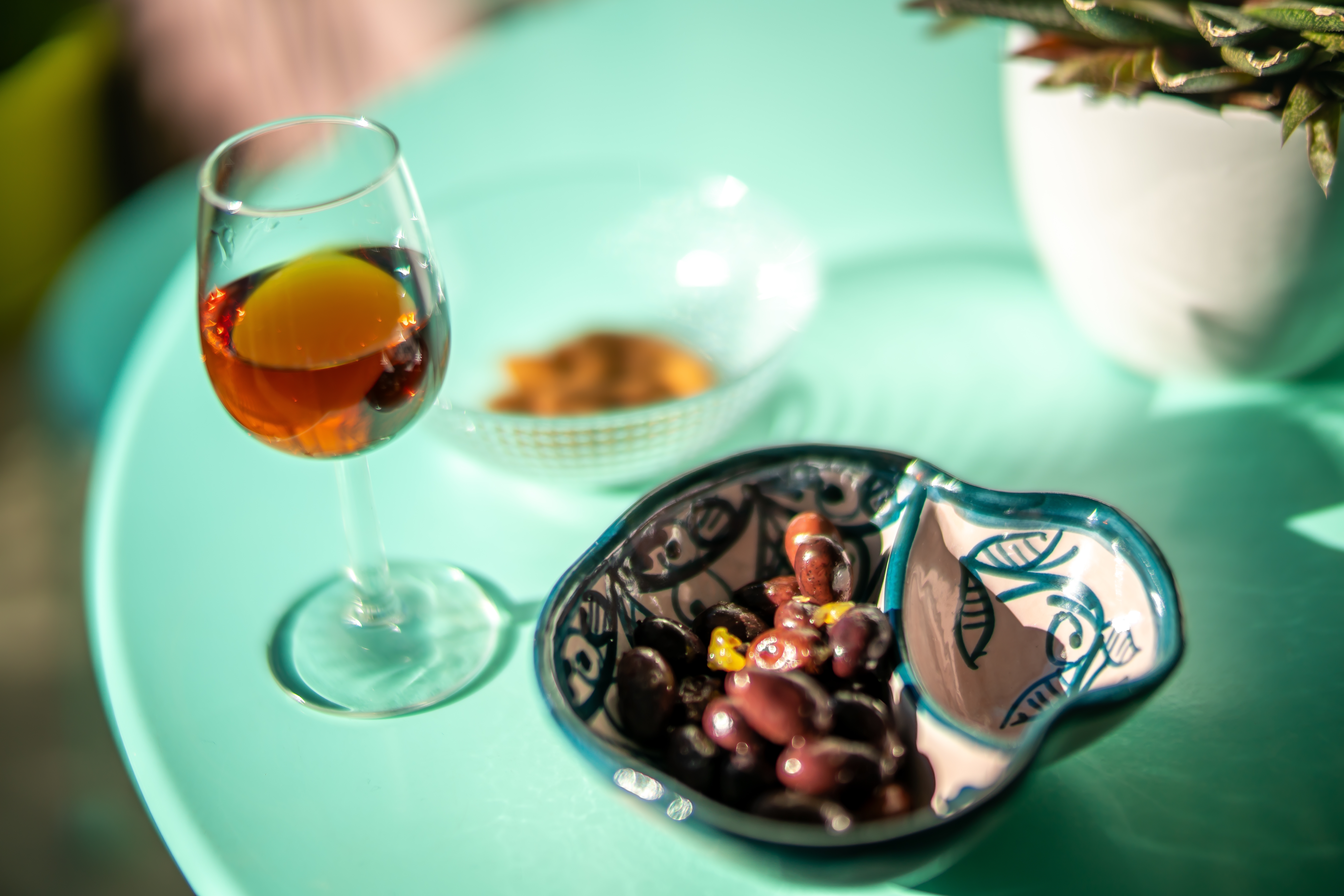 A glass of sherry and a dish of olives rest on a turquoise table in Seville, Spain.